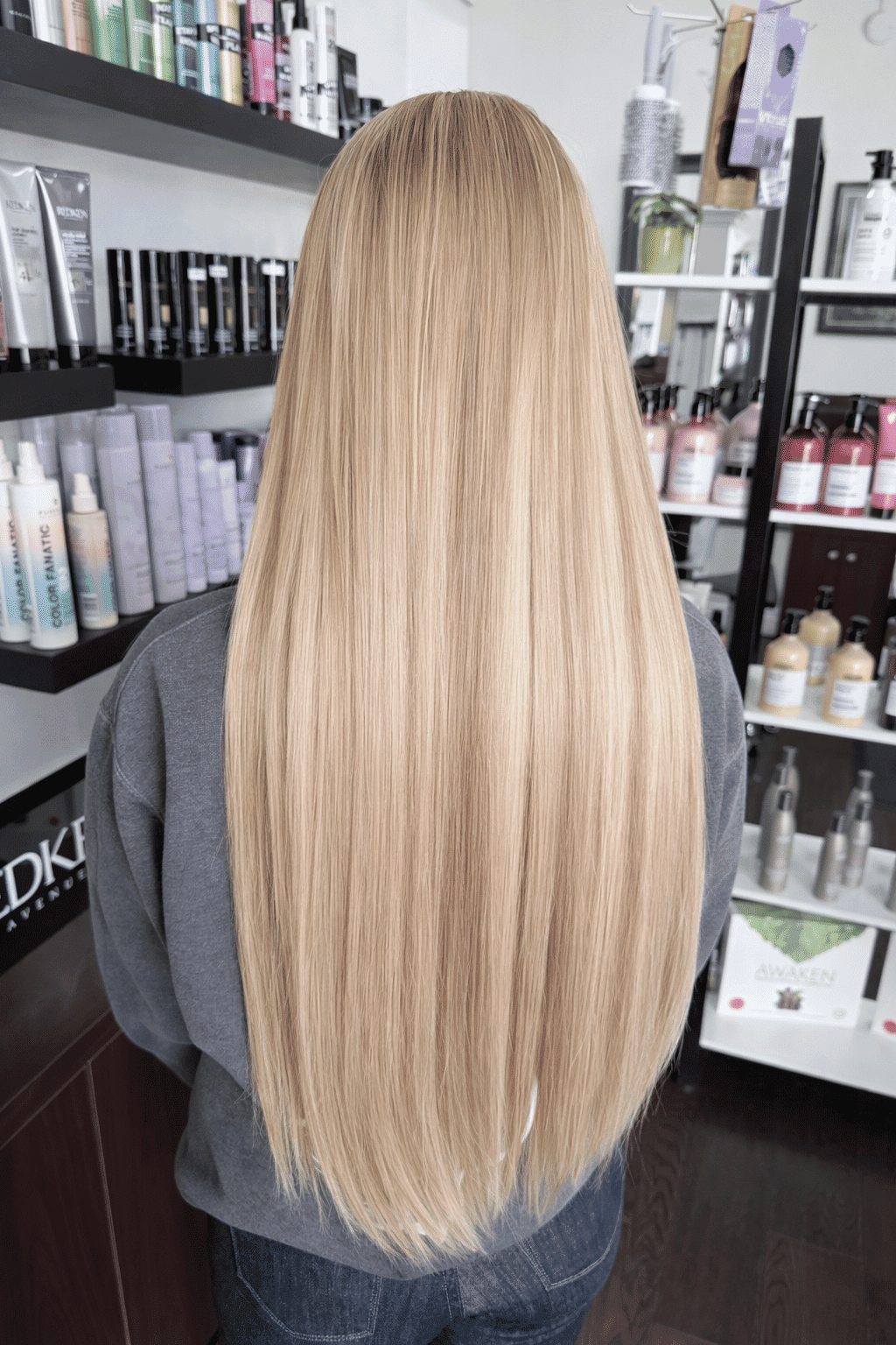 Long blonde hair in salon with various hair products on shelves.