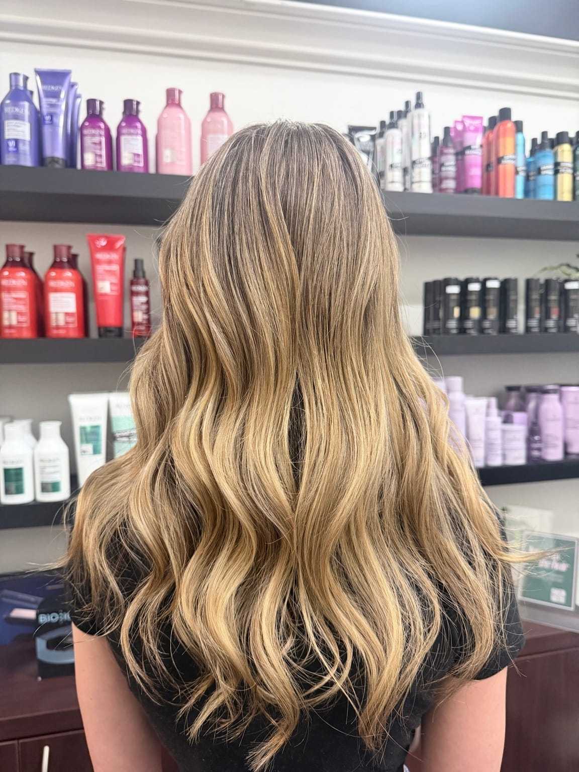 Blonde hair with waves in a salon, shelves of hair products in the background.